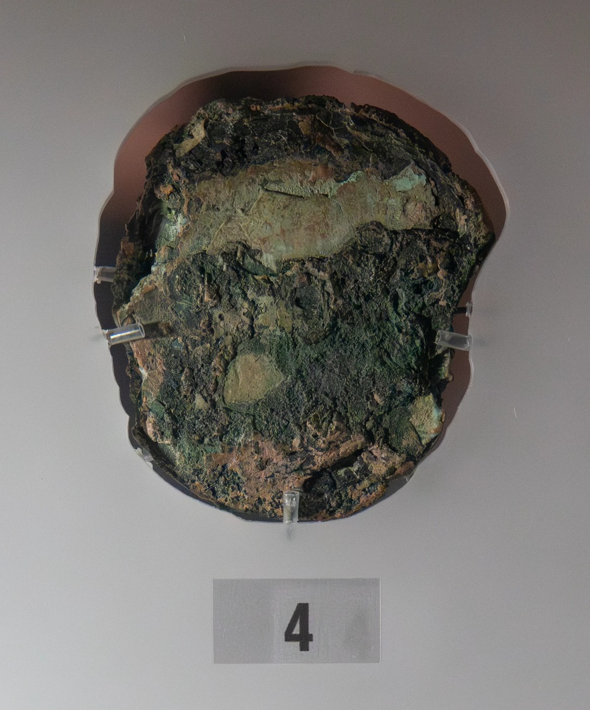 Figure 4 — Fragment D in its display mount at the National Archaeological Museum, Athens: a single corroded gear, once thought to be two, with a disk riveted to it. Tomography gives 63 teeth. The UCL team rea…