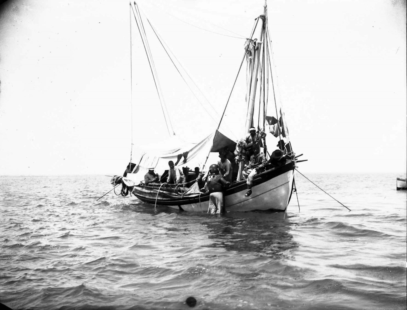 Figure 1 — Sponge divers at the Antikythera wreck during the salvage of 1900–1901. One diver, in standard diving dress with its heavy copper helmet, stands in the water at the side of the anchored boat; anoth…