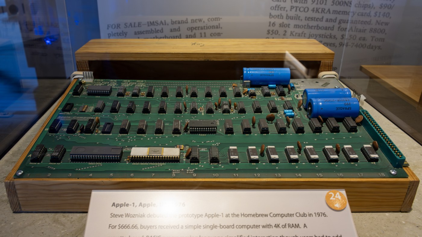 Figure 7 — The Apple-1 on display at the Computer History Museum, Mountain View, in its exhibition "Revolution", photographed in 2023. The board sits in a home-made wooden case, as many did. The museum label …