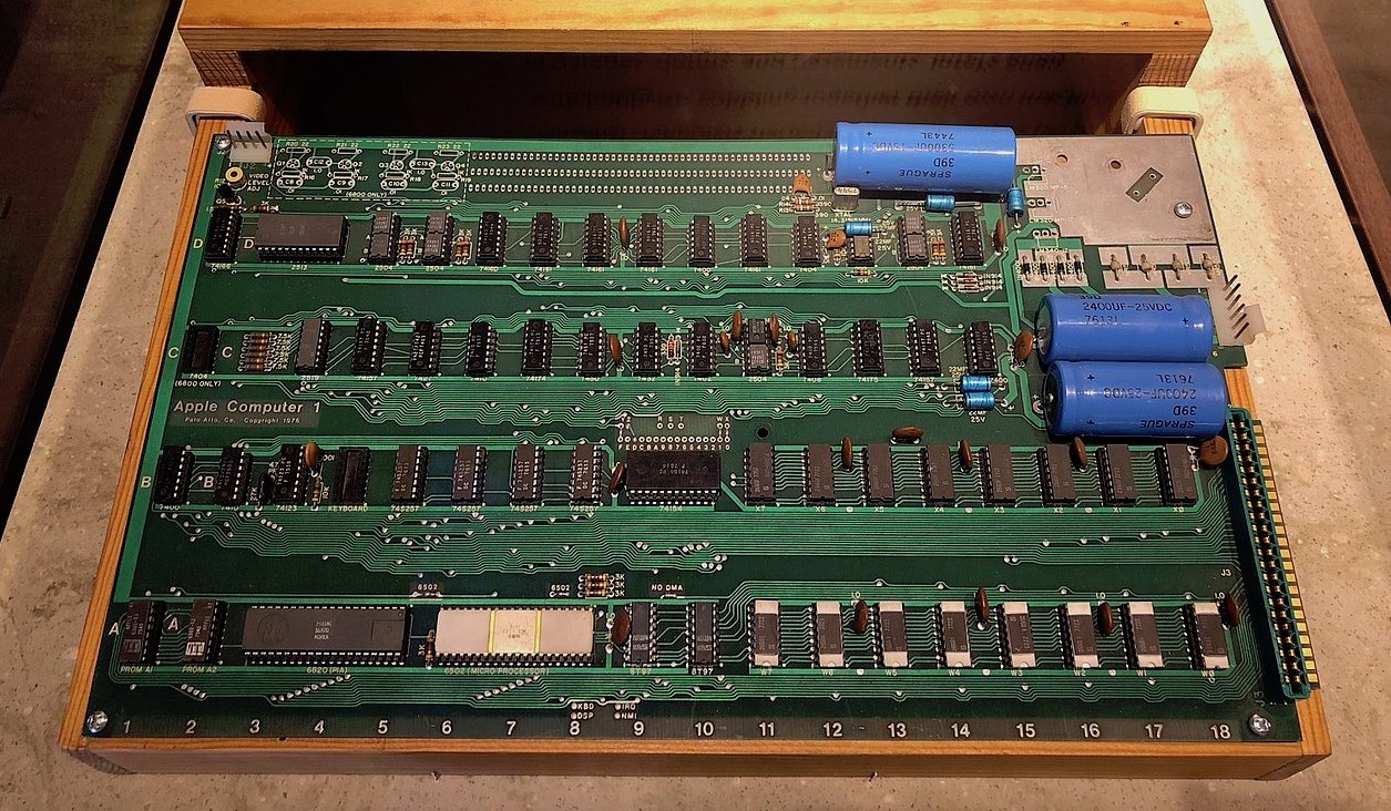 Figure 1 — An Apple-1 board in its wooden case at the Computer History Museum, Mountain View (the Commons file identifies it as Wozniak's). The column numbers 1 to 18 run along the bottom edge; the rows A to …