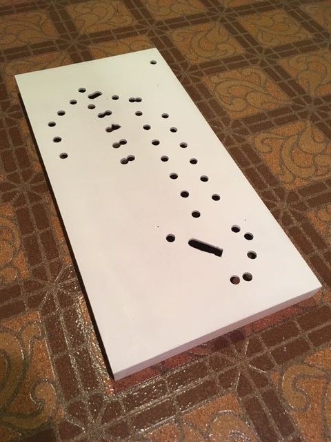 Figure 3 — The finished base box before the parts go on: the plywood panel painted white under the printed top deck, with the openings drilled and sawn through for the holes that balls drop into and for the r…