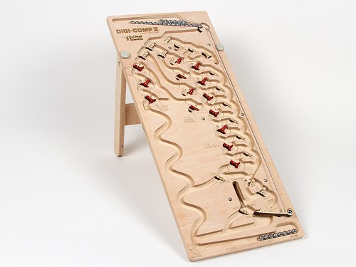 Figure 4 — Evil Mad Scientist's Digi-Comp II: First Edition (2012) on its stand: a CNC-carved, laser-engraved maple-plywood board, 10 by 24 inches, with red-and-black plywood flip-flops pivoted on brass pins …