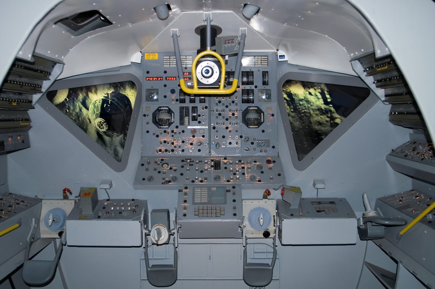 Figure 4 — A Lunar Module cockpit mock-up; the LM carried a single DSKY between the two crew stations. File:Lunar Module Simulator.jpg by Stuart Seeger from College Station, Texas, USA. License: CC…