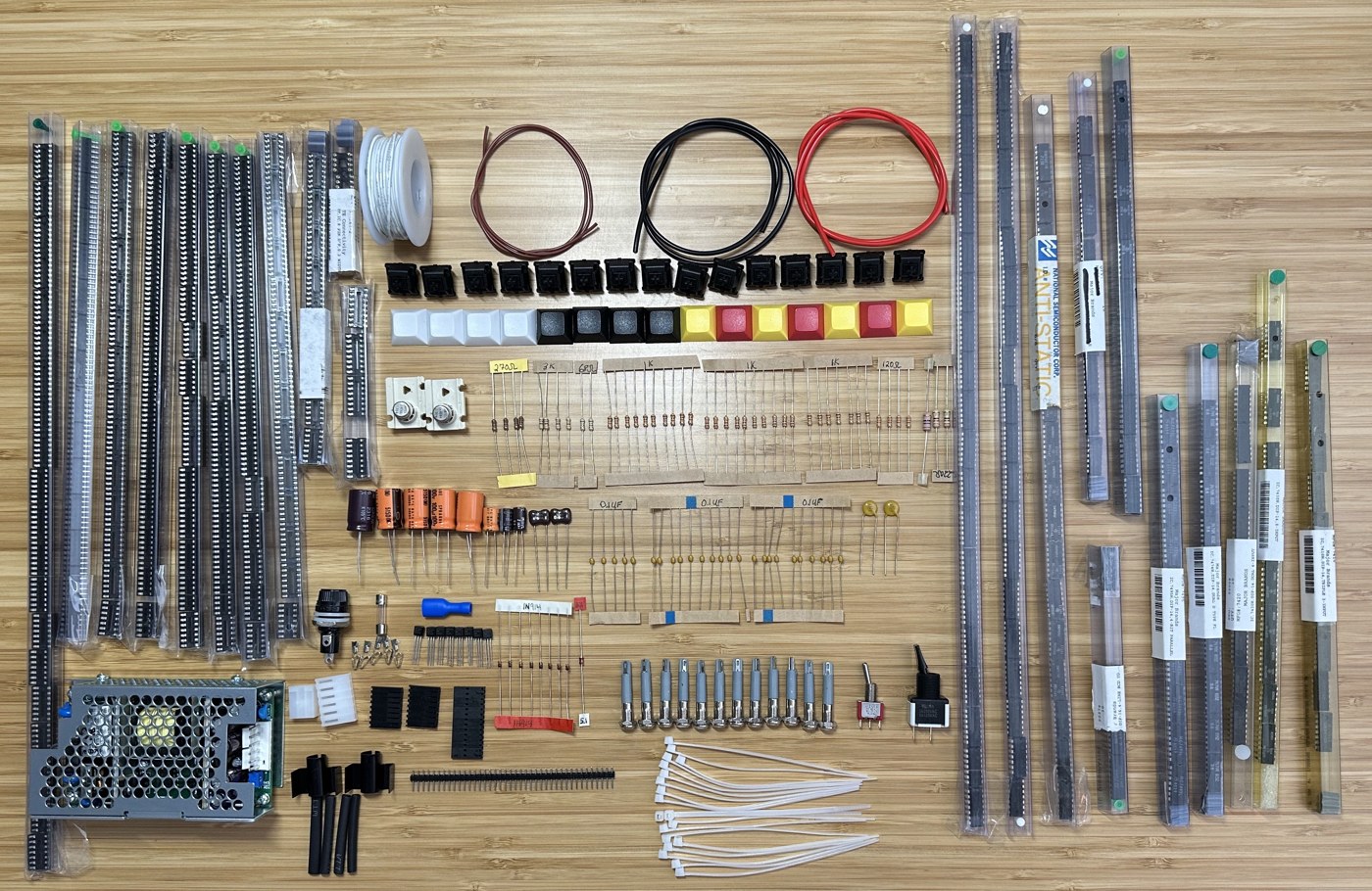 Figure 4 — The parts of Artem Kalinchuk's KENBAK-1 reproduction kit laid out: tubes of TTL chips and DIP sockets, keyswitches and black, white, red and yellow keycaps, resistors, capacitors, the switching pow…