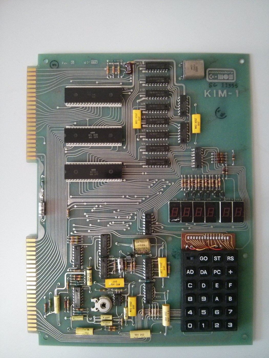 Figure 1 — A Commodore-era KIM-1: the 6502 and two 6530s down the left, the column of eight 1-kilobit memory chips, the six LED digits and the 23-key keypad at lower right. Learning machine code on a KIM mean…