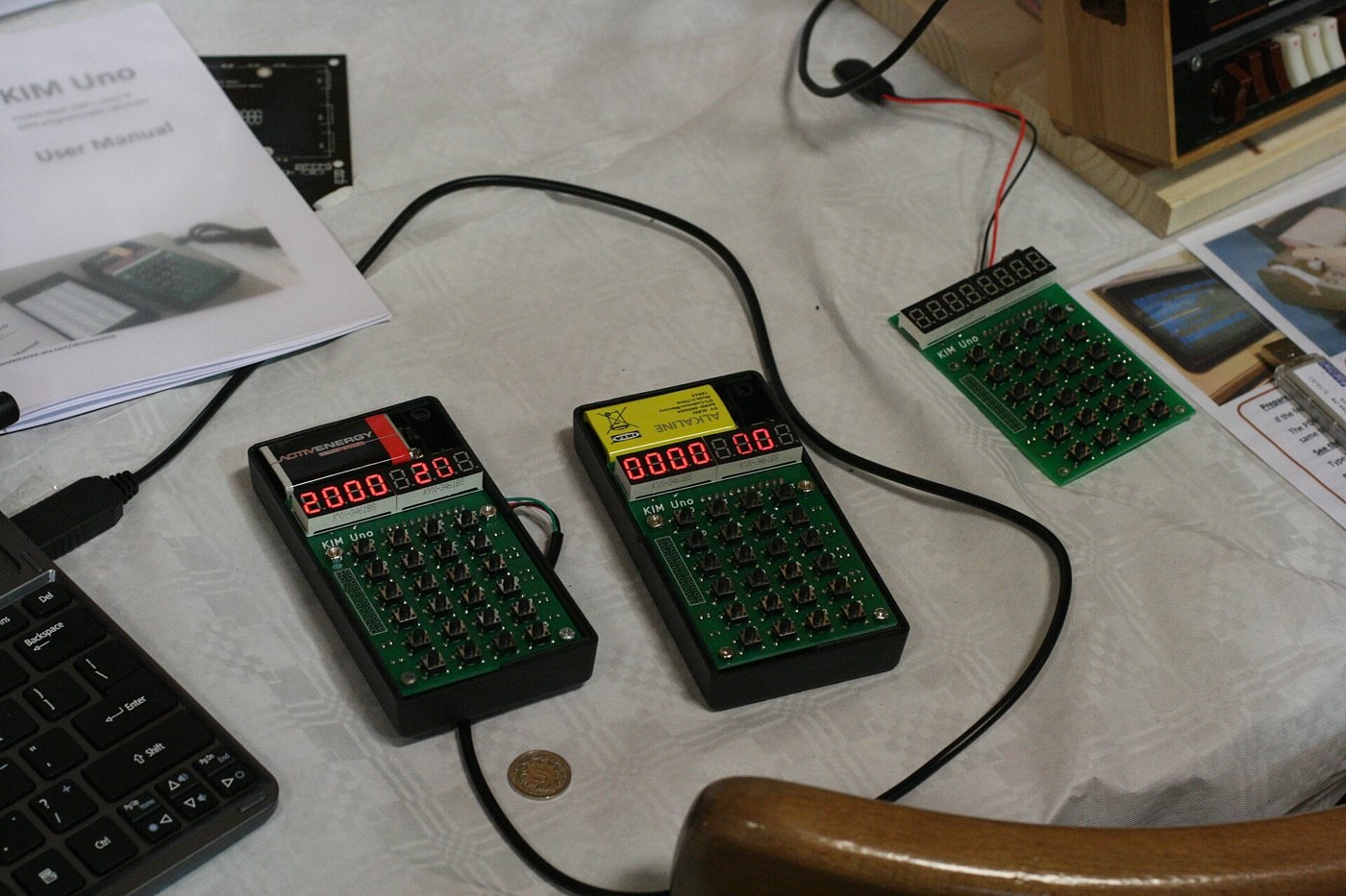 Figure 6 — Three KIM Unos at a show, two of them running. Oscar Vermeulen's KIM Uno puts a KIM-1 emulator on an Arduino Pro Mini behind a small board with 24 keys and a calculator-style LED display; it runs t…
