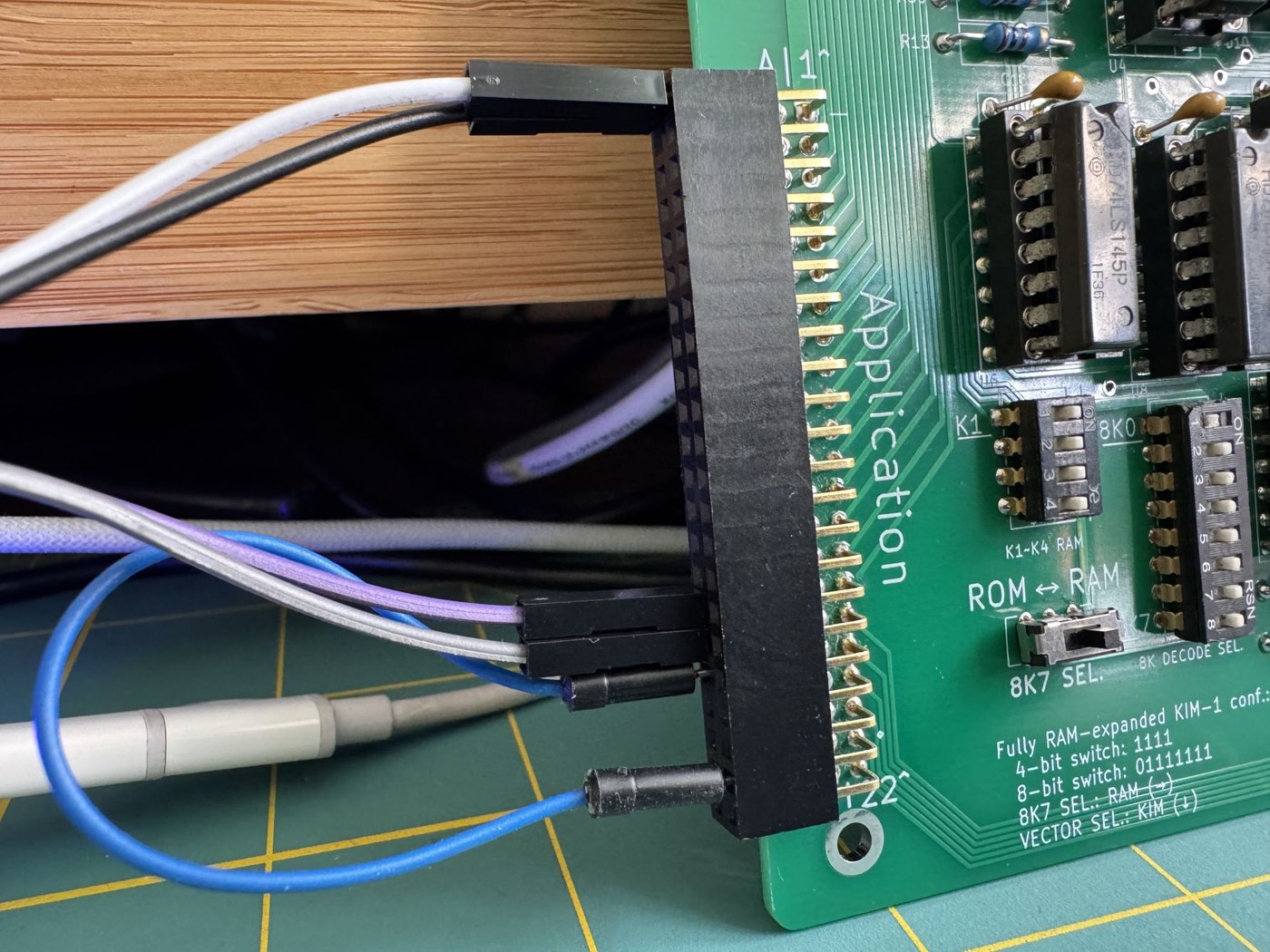 Figure 6 — The Application connector on a working PAL-2, with jumper wires from the USB-to-TTL adapter pushed onto the header. The silkscreen in the corner records the "Fully RAM-expanded KIM-1" switch settin…