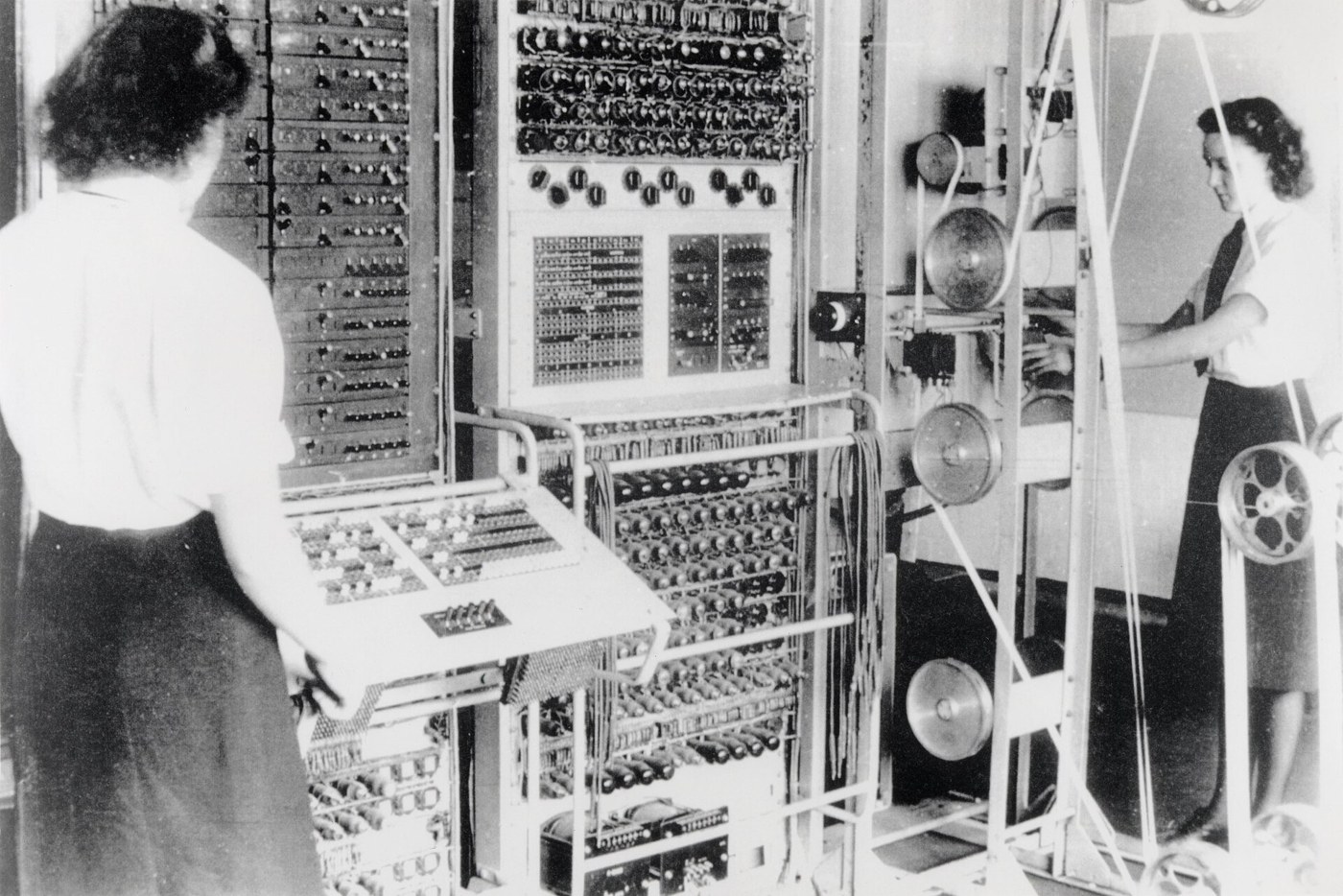 Figure 1 — A Colossus Mark 2 at Bletchley Park, operated by Dorothy Du Boisson (left) and Elsie Booker of the Women's Royal Naval Service. On the right is the bedstead carrying the single loop of message tape…