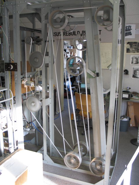 Figure 4 — The bedstead of the rebuilt Colossus at Bletchley Park, seen from the end. The tape loop runs round the large pulleys at top and bottom; the reader is at the left. On the original machines the oper…