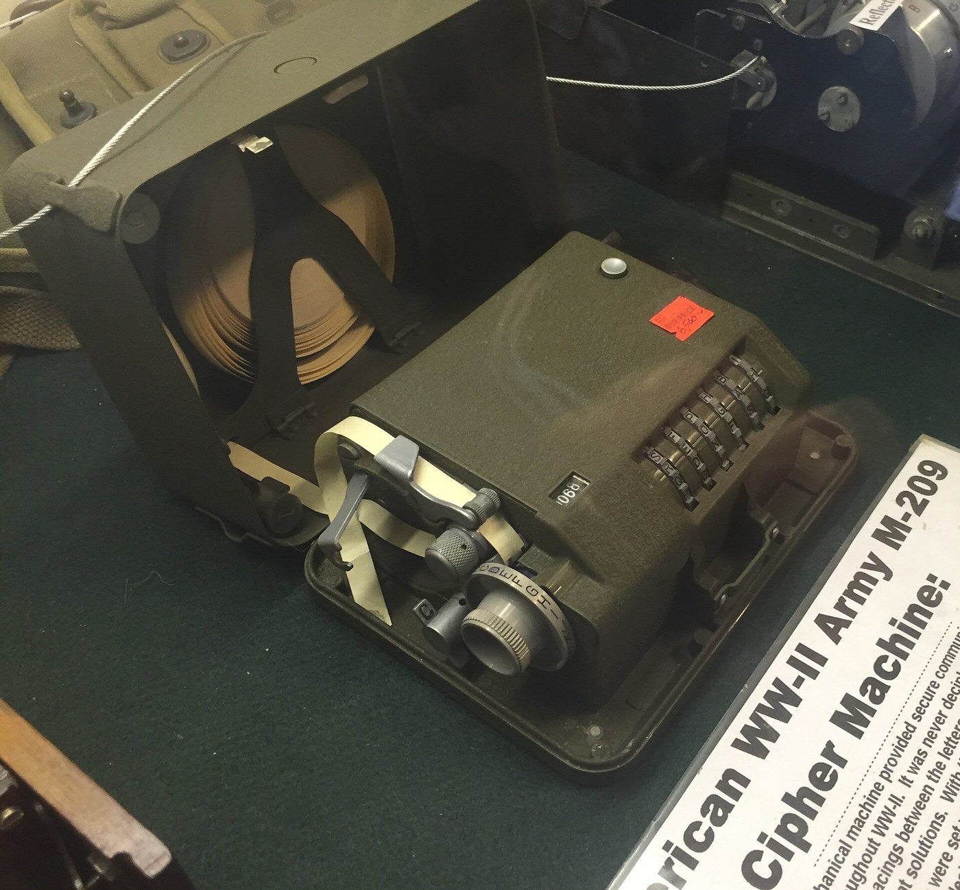 Figure 2 — An M-209 seen from the left side: the setting knob and indicating disk, the paper-tape guides and pressure roller, and the letter-counter window. The replica keeps this arrangement — letter in at t…