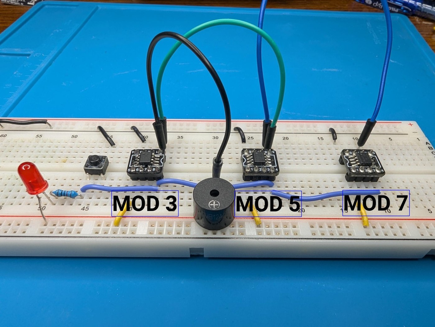 Figure 3 — Build 01: three ATtiny412s on a breadboard holding moduli 3, 5 and 7, with a push button to step them and a piezo buzzer on the shared reject line. Each rejection is a click; the silences are the c…