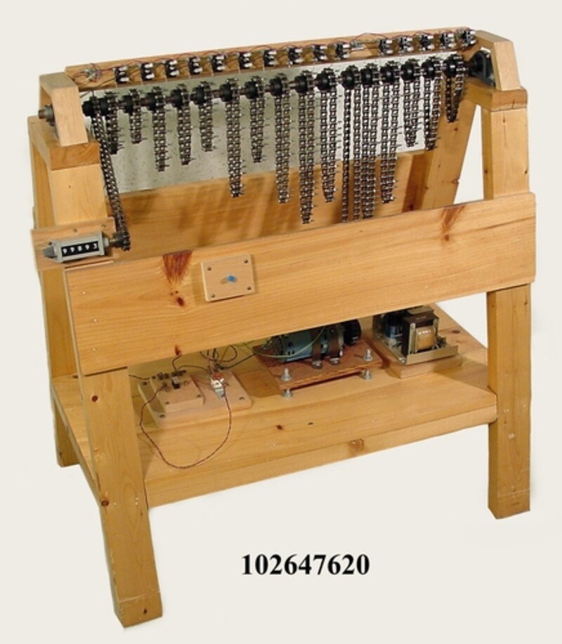 Figure 5 — The Computer History Museum's reproduction of the chain sieve, built in 1981. A sawhorse-shaped wooden frame carries a shaft of sprockets at the top: one sprocket drives from a motor at the bottom,…