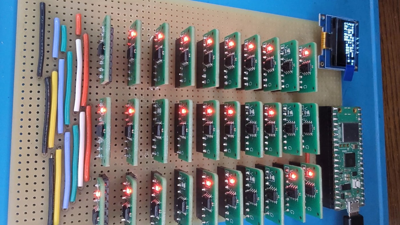 Figure 7 — The finished Tiny Sieve: thirty modulus cards in three rows of ten on a stripboard backplane, the Raspberry Pi Pico at the right edge and the OLED status display beside it. Each card's LED lights w…